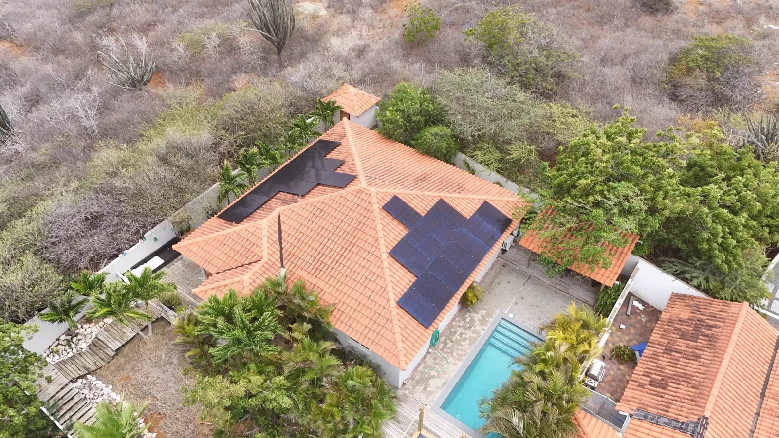 Dronefoto van zonnepanelen op meerdere dakvlakken van een villa met zwembad op Curaçao